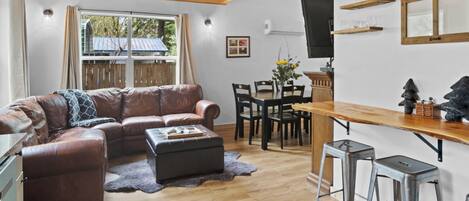 Una sala de estar acogedora con un sofá de cuero marrón, una mesa de comedor de madera y una zona de bar con taburetes.