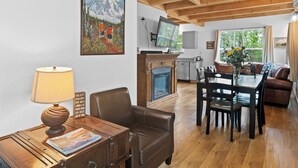 A cozy living room with a fireplace, wooden furniture, and a painting of a mountain scene.