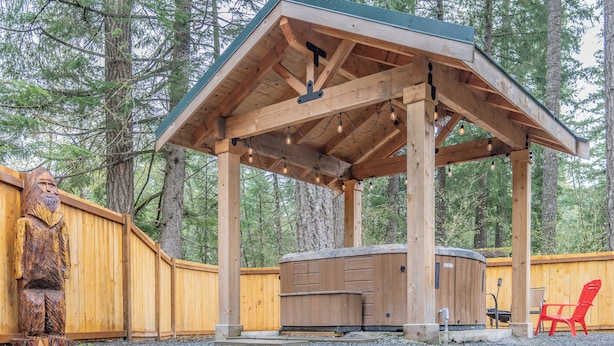 A wooden gazebo with a hot tub, surrounded by a wooden fence and a wooden sculpture.
