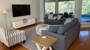 Een moderne woonkamer met een flatscreen televisie, een grijze bank, gestreepte fauteuils en een houten salontafel.
