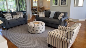 Een moderne woonkamer met twee banken, een gestreept fauteuil, een gestreept voetenbankje en een kleine tafel.