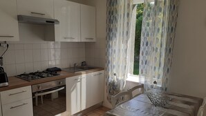 A kitchen with white cabinets, a gas stove, a sink, and a window with patterned curtains.
