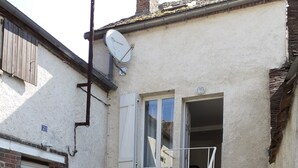 A residential building with a staircase leading to a second floor, a satellite dish, a potted plant, and a brick wall.