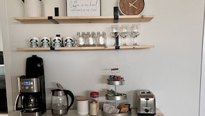 Una cocina con cafetera, tostadora, frascos y un reloj en la pared.