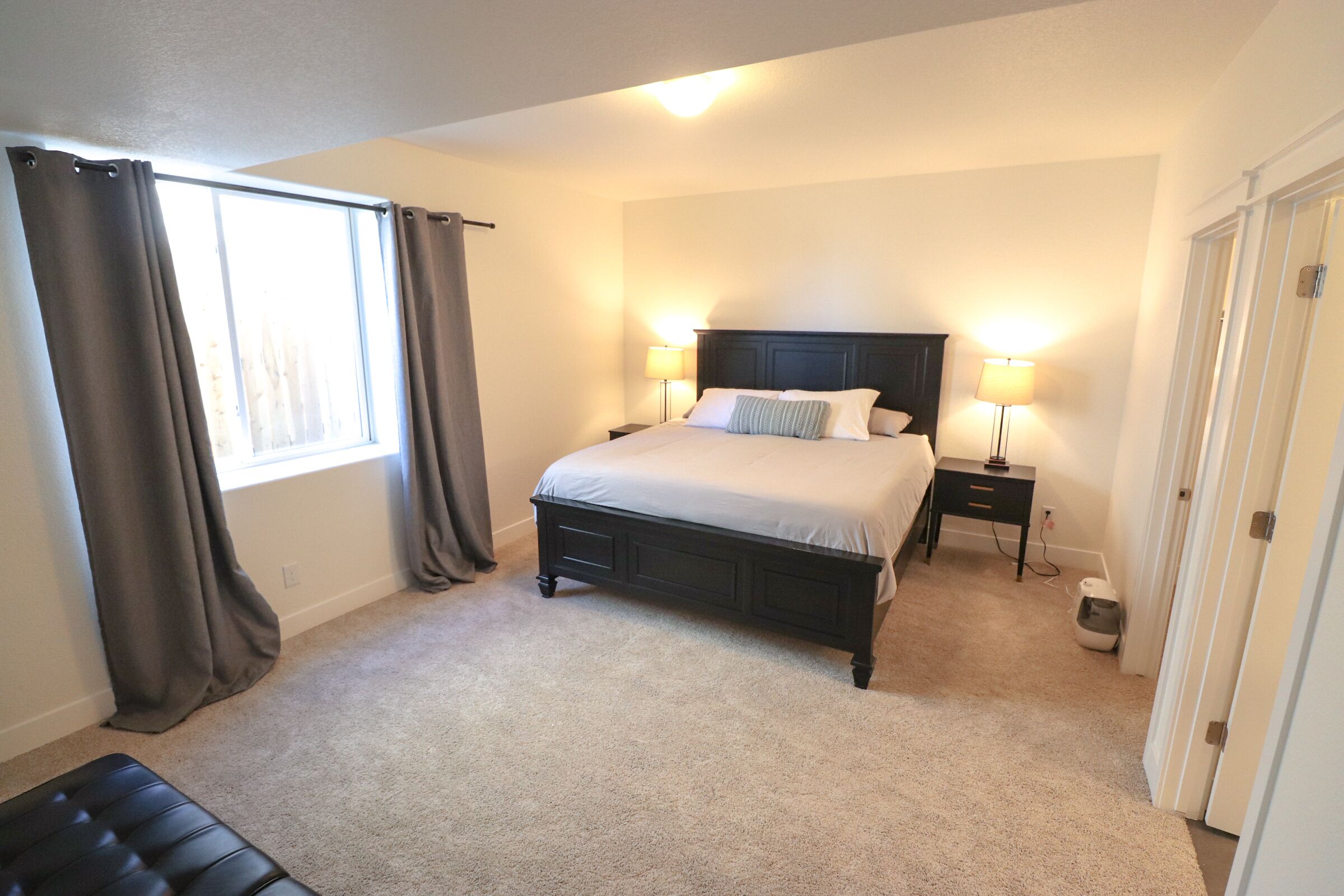 A bedroom with a bed, bedside tables, a lamp, a waste bin, and a window with curtains.