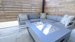 Un área de estar al aire libre con diseño moderno, que incluye un brasero integrado y un muro de fondo de madera.