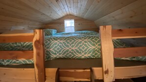 A cozy attic bedroom with wooden walls and a sloped ceiling. There are two bunk beds with patterned bedding.