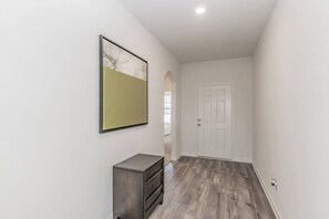 Un pasillo con una puerta blanca, un archivador pequeño y un cuadro en la pared.