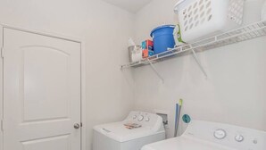 A laundry room with a washing machine, dryer, and shelves with laundry supplies. - Modern Spacious 4BR New Built Retreat ~ Fam&Group (Seagoville)