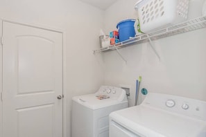 A laundry room with a washing machine, dryer, and shelves with laundry supplies. - Modern Spacious 4BR New Built Retreat ~ Fam&Group (Seagoville)