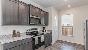 A modern kitchen with dark cabinets, stainless steel appliances, and a granite countertop. - Modern Spacious 4BR New Built Retreat ~ Fam&Group (Seagoville)