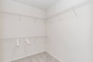 A room with white walls and a carpeted floor, featuring two wire shelving units against the walls.