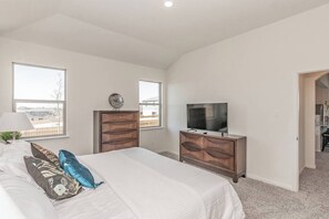 Un dormitorio con una cama grande, dos cómodas de madera, un televisor y un ventanal con vistas.