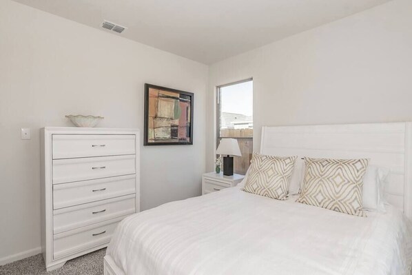 A bedroom with a bed, a dresser, a nightstand, a lamp, and a window.