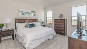 A bedroom with a large bed, a nightstand with a lamp, a dresser, and a TV on a desk. - Modern Spacious 4BR New Built Retreat ~ Fam&Group (Seagoville)