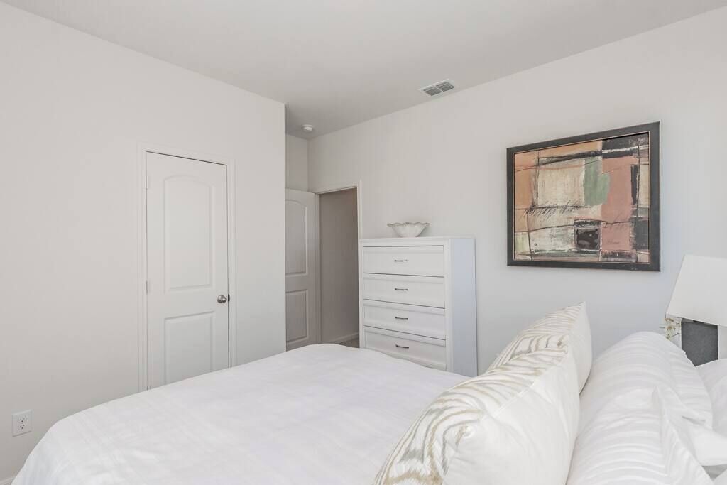 Una camera da letto con un letto, una cassettiera, una porta e un quadro appeso al muro.