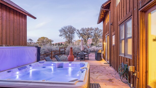 Un bain à remous dans un espace extérieur en bois, agrémenté d’une terrasse, d’une clôture en bois et offrant une vue sur les arbres et les collines en arrière-plan.