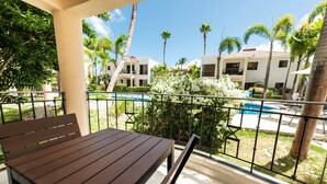 A balcony with a wooden table and chairs, overlooking a swimming pool and palm trees. - Recently refurbished, five star facility (El Cortiesito-)