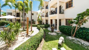 A multi-story hotel with balconies, a well-maintained garden with palm trees and hedges, and outdoor seating areas. - Recently refurbished, five star facility (El Cortiesito-)