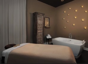 Quarto moderno com uma cama grande, um guarda-roupa de madeira, uma mesinha com toalhas, um espelho fixado na parede e uma banheira.