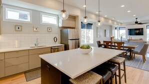 A modern kitchen with a central island, pendant lights, and a dining area with a TV. - Panoramic View- 8 Comfy Beds - Multilevel Townhome (Nashville)