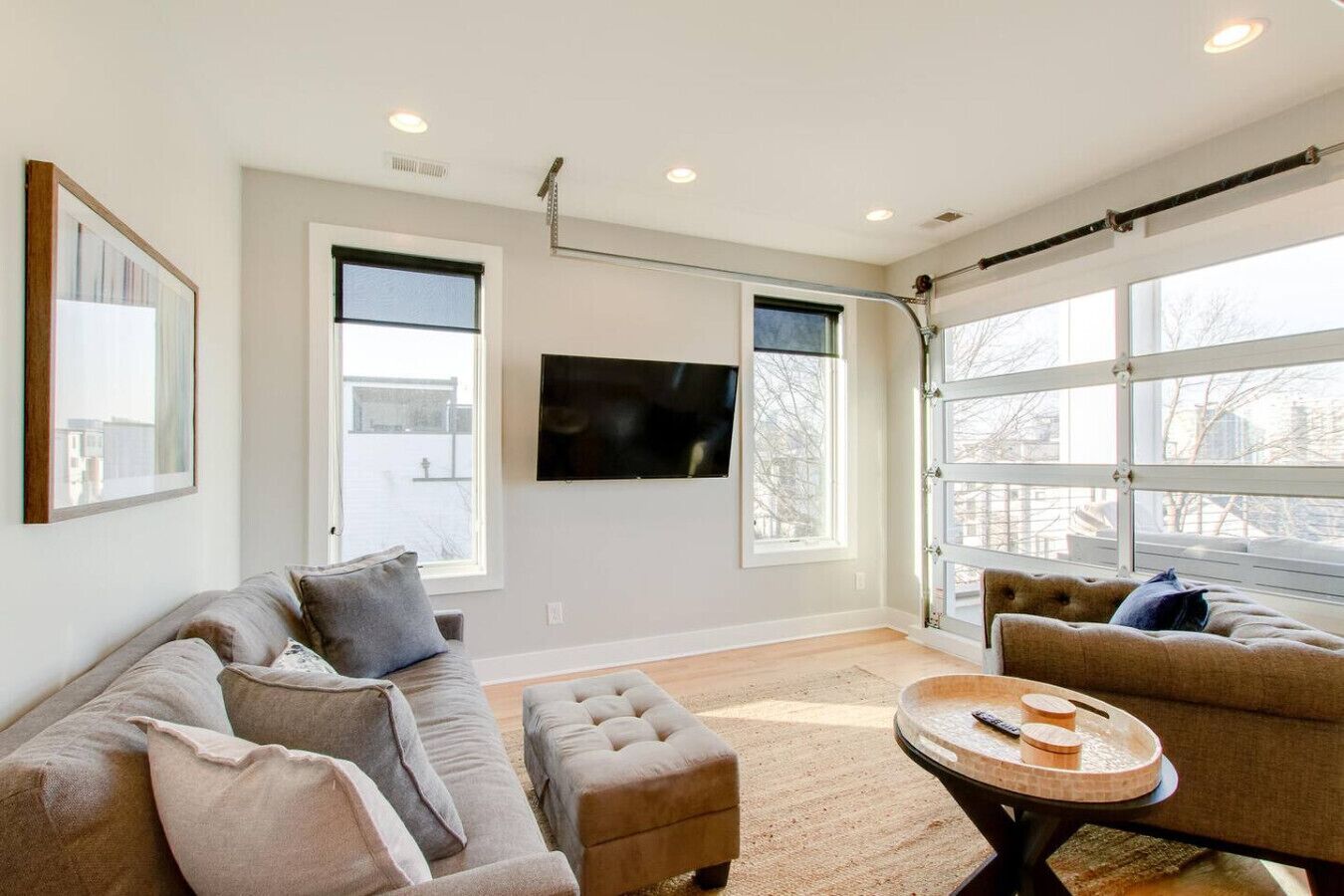 A spacious living room with a large window, a flat-screen TV, and a round coffee table.