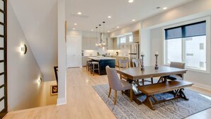 A modern kitchen with a central island, a dining area with a wooden table and chairs, and a staircase leading to another level. - Panoramic View- 8 Comfy Beds - Multilevel Townhome (Nashville)