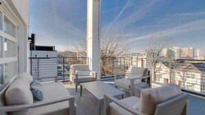 A balcony with white furniture, including sofas and chairs, overlooking a cityscape with buildings and bare trees. - Panoramic View- 8 Comfy Beds - Multilevel Townhome (Nashville)
