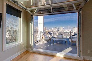 Un apartamento moderno con un amplio ventanal corredero que da a un balcón con mobiliario exterior.
