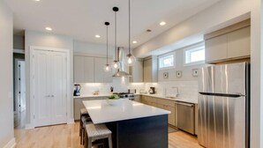 A modern kitchen with a central island, stainless steel appliances, pendant lighting, and a view of the adjacent living area. - Panoramic View- 8 Comfy Beds - Multilevel Townhome (Nashville)