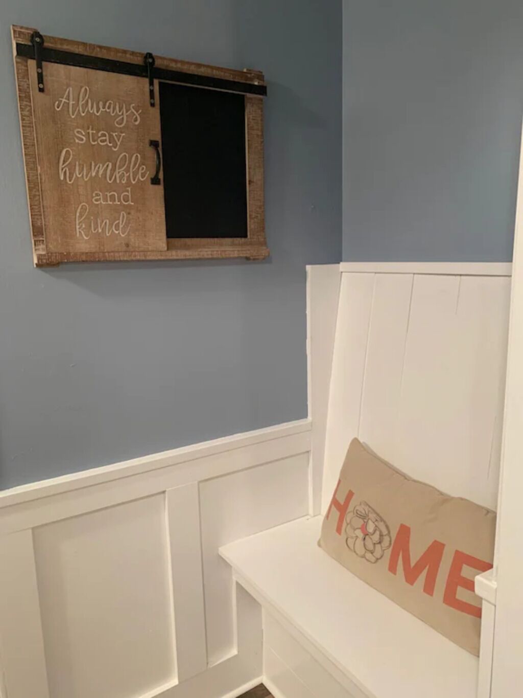 Ein Zimmer mit blauer Wand, einem Holzschild mit einem motivierenden Spruch, einer weißen Bank und einem Kissen mit dem Wort 'HOME'.