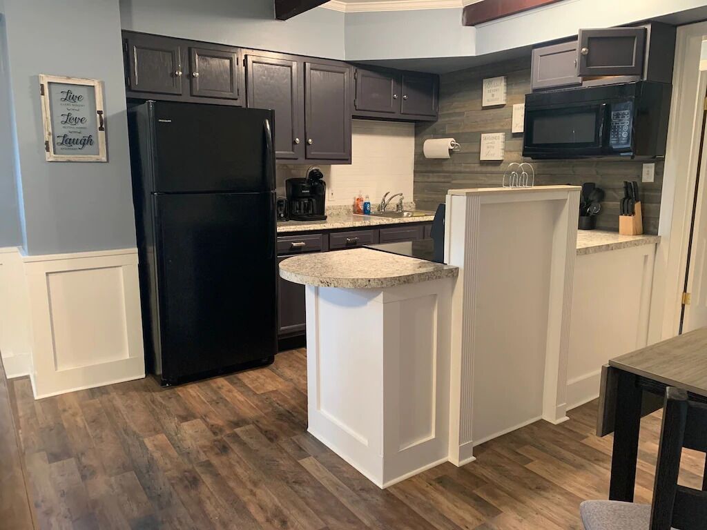 A compact kitchen with dark cabinets, a black refrigerator, a microwave, and a small island with a countertop.