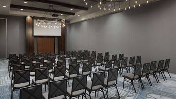 A conference room with rows of chairs, a large screen, and a modern chandelier.