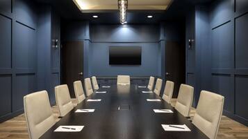A conference room with a long table, beige chairs, a flat-screen TV on the wall, and recessed lighting.