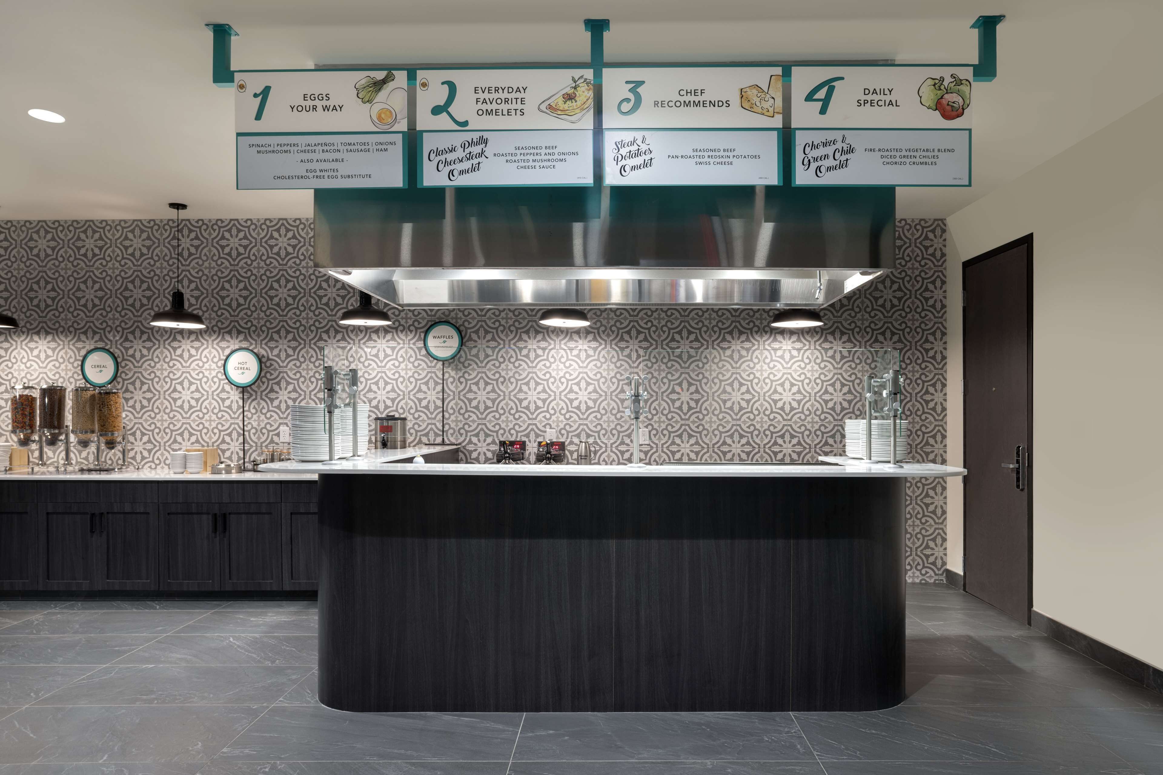 A modern kitchen with a central island, a patterned backsplash, and a menu board above displaying four breakfast options.