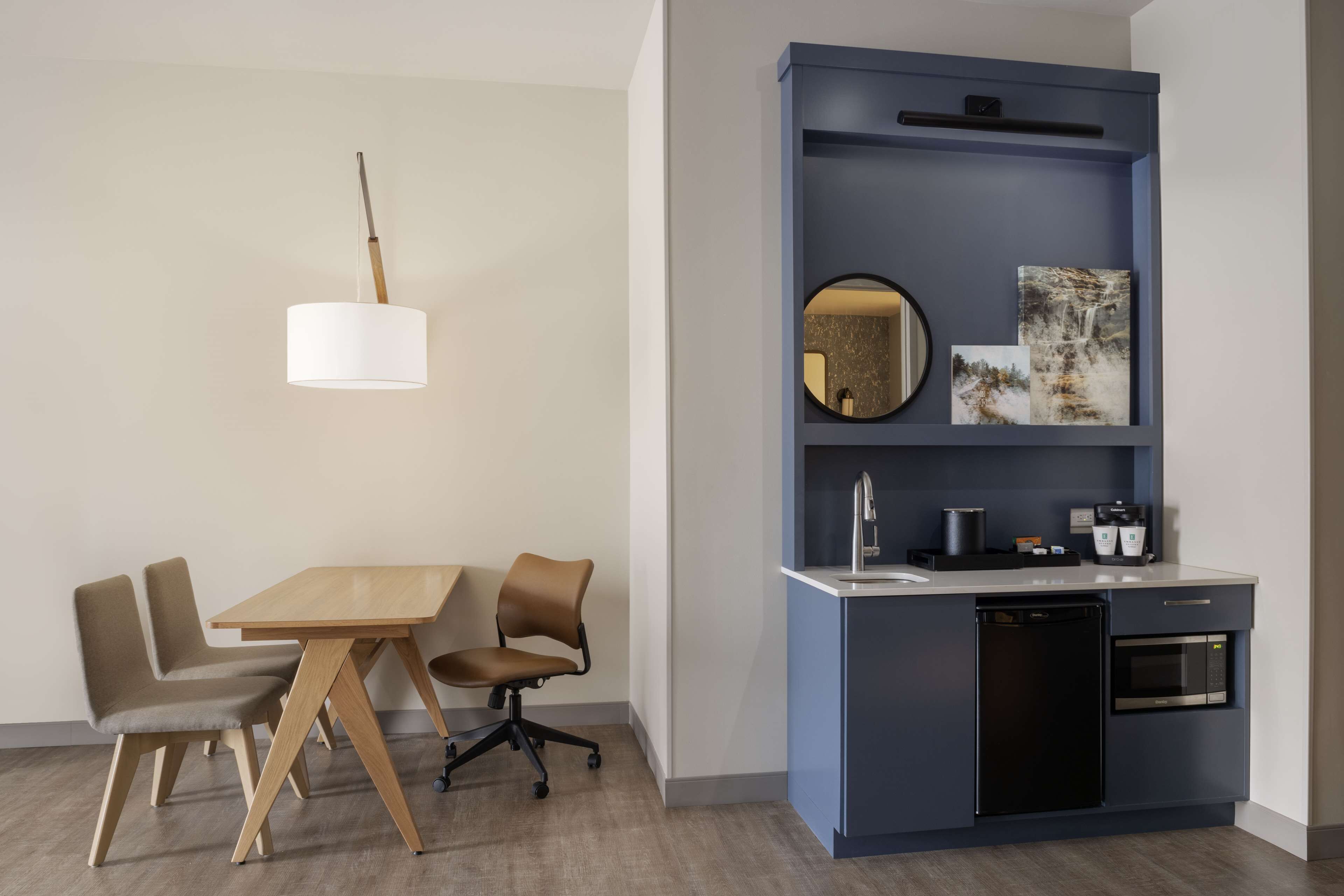 A modern kitchen with a blue cabinet, a round mirror, and a coffee machine.