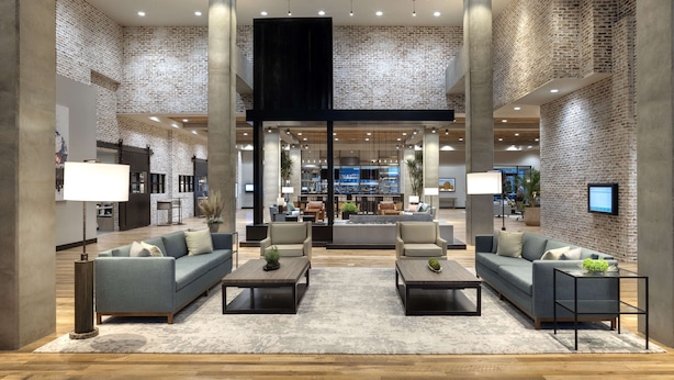 A spacious lobby with a brick wall, a central seating area with sofas and coffee tables, and a modern design with exposed brick and concrete pillars. - Embassy Suites by Hilton Bowling Green (Bowling Green)