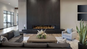 A modern living room with a fireplace, leather sofas, and a coffee table with a floral arrangement. - Embassy Suites by Hilton Bowling Green (Bowling Green)