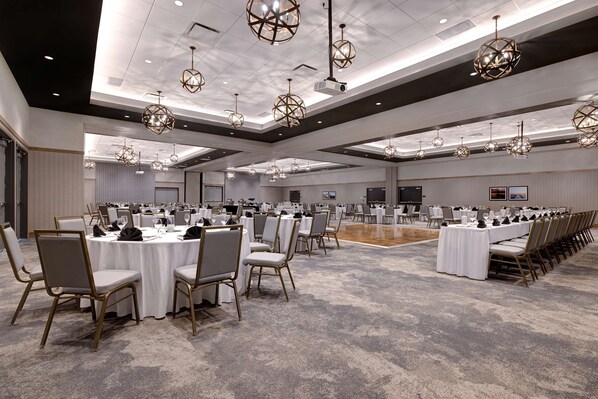 A spacious banquet hall with multiple round tables, each set with white tablecloths and chairs, and geometric pendant lighting.