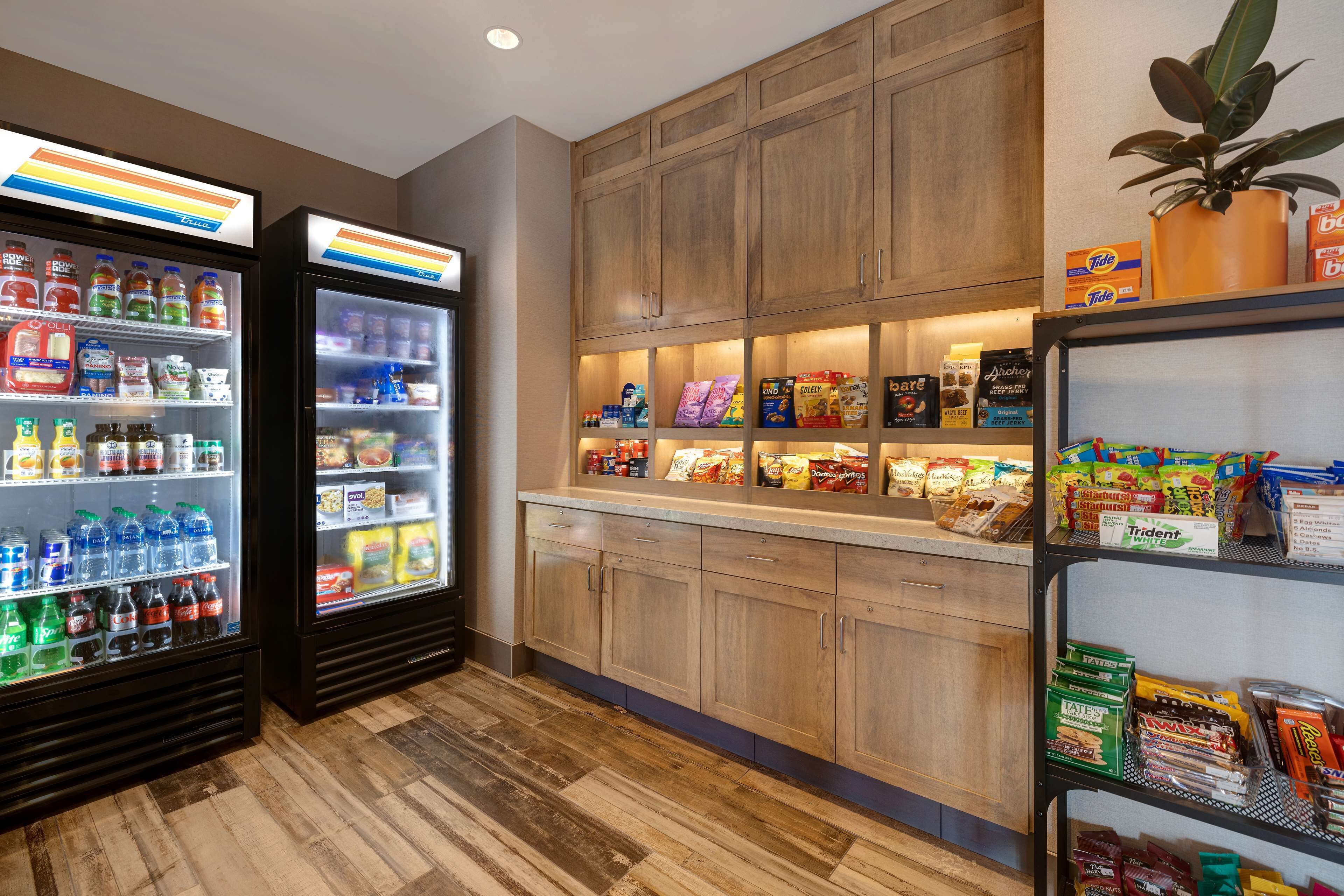 Una kitchenette con dos dispensadores de bebidas, armarios de madera y estantes llenos de aperitivos y condimentos.