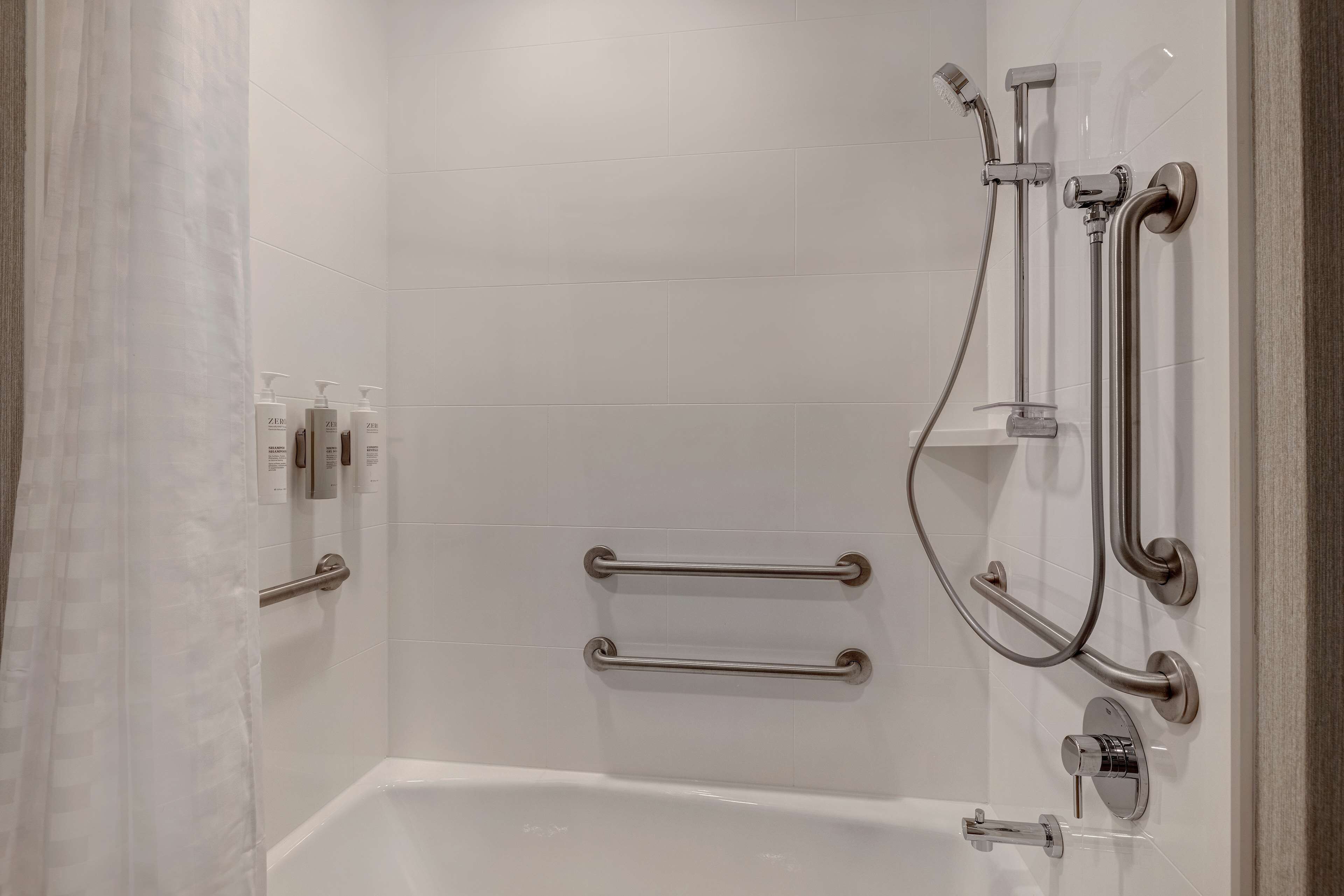 A modern bathroom with a white bathtub, grab bars, and a shower with a handheld showerhead.