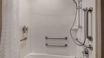 A modern bathroom with a white bathtub, grab bars, and a shower with a handheld showerhead.