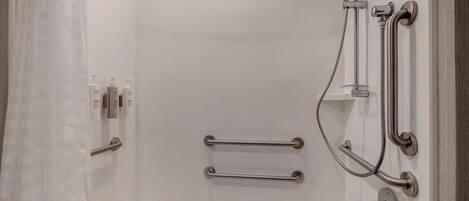 Un baño moderno con una bañera blanca, barras de apoyo y una ducha con cabezal de ducha manual.