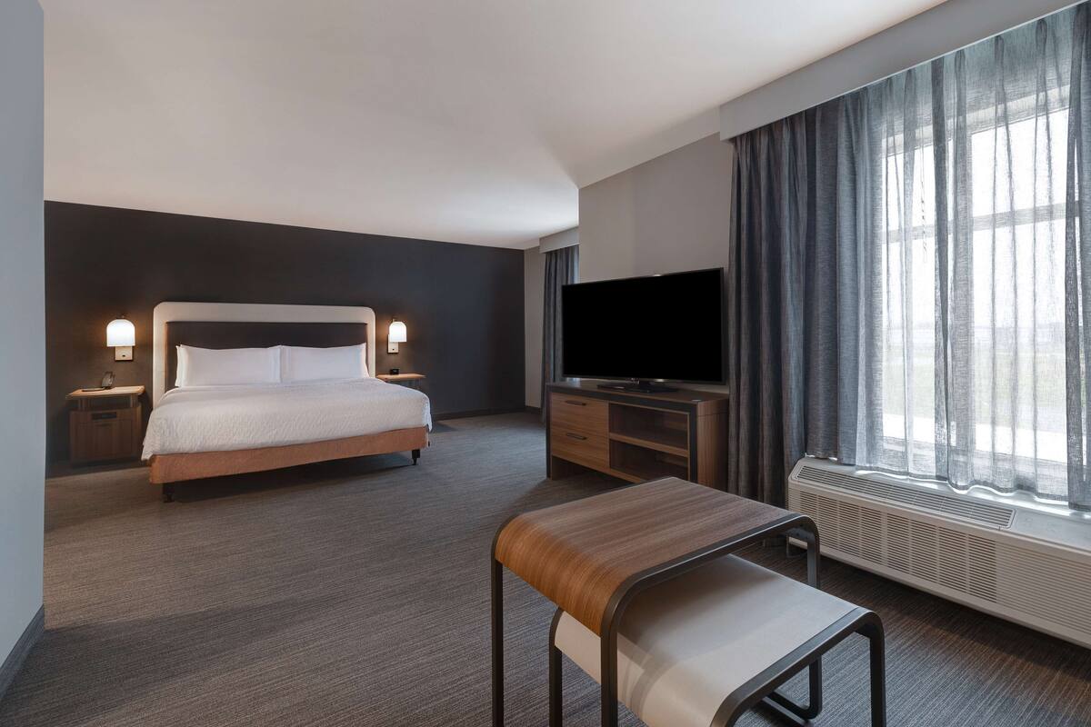 Una habitación de hotel con cama, televisión, escritorio y ventana con cortinas.