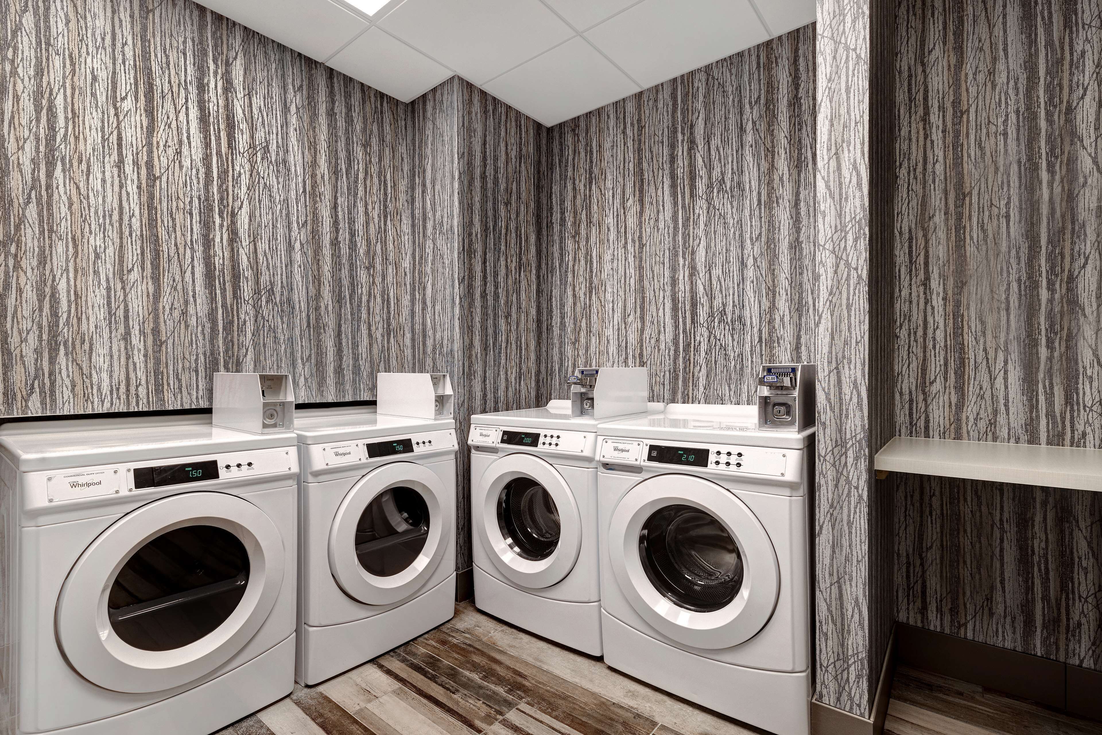 A laundry room with three front-loading washing machines, a drying rack, and a wooden floor.