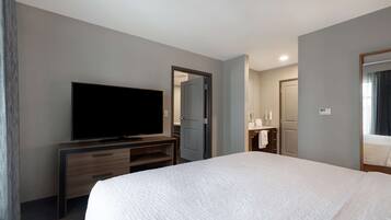 A hotel room with a large bed, a TV on a wooden stand, a bathroom with a mirror, and a door leading to another room.