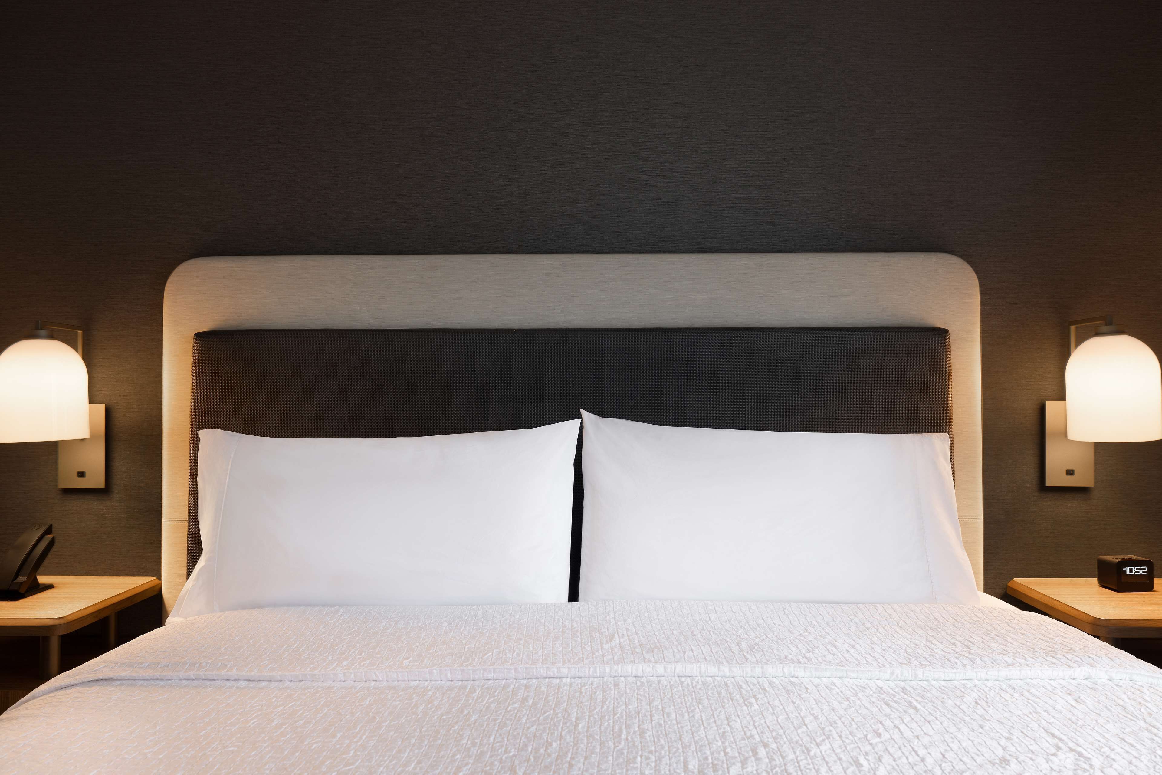 A neatly made bed with white linens, a dark headboard, and two bedside lamps on either side.