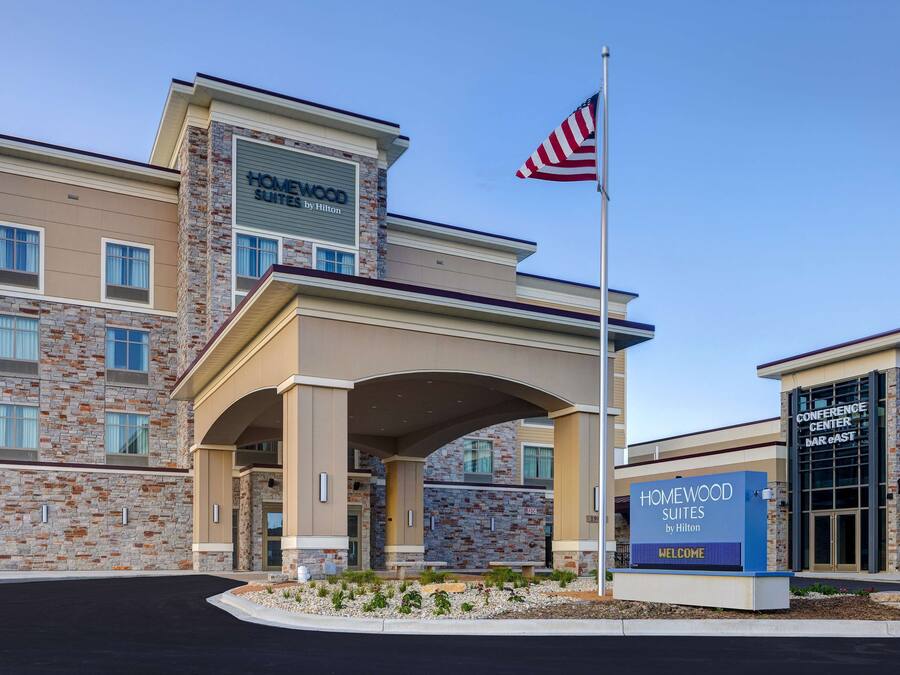 A hotel entrance with a stone facade, a large American flag, and a sign welcoming guests.