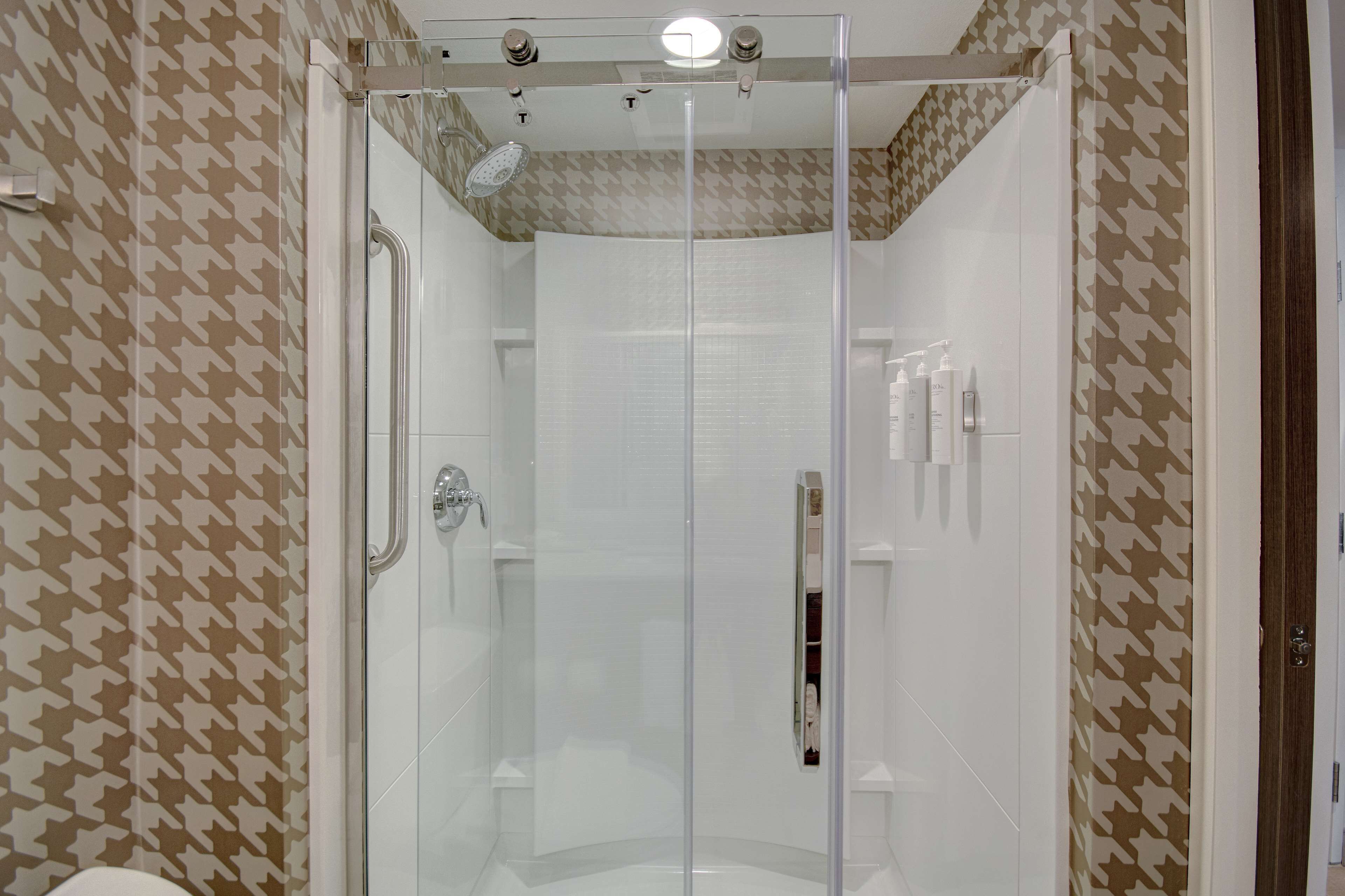 Une salle de bain moderne avec une douche à parois de verre, des murs recouverts de carreaux blancs et un papier peint à motifs.