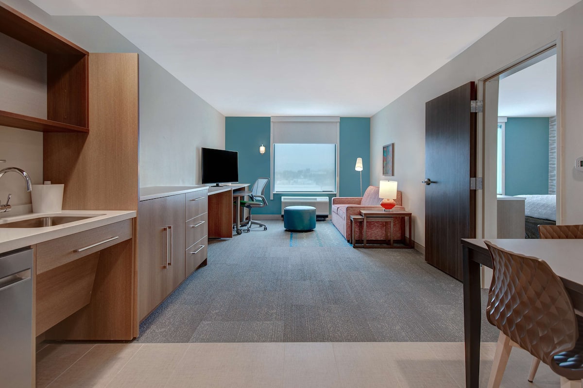 Une chambre d’hôtel moderne dotée d’une kitchenette, d’un coin repas et d’un espace salon offrant une vue sur la ville.